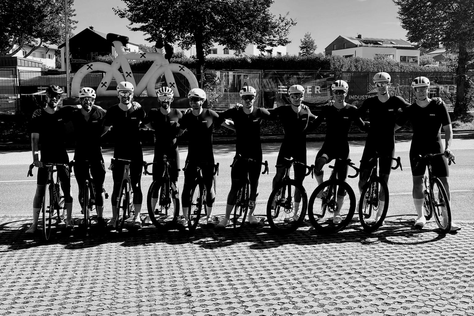 Ten riders in black Stay Average kit standing in a row with their road bikes.
